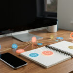 Bureau créatif avec ordinateur, smartphone, carnet et icônes abstraites de contenus reliées par des lignes lumineuses.