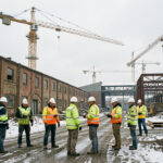 Vue documentaire d’une ancienne friche industrielle française en reconversion, avec des ouvriers, des grues et des bâtiments industriels sous une lumière hivernale.